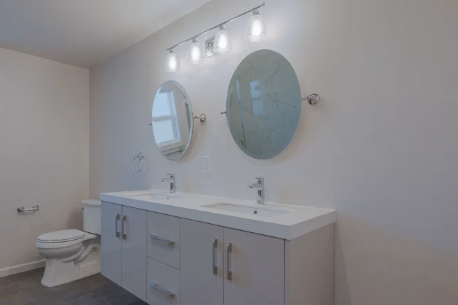 A double sink vanity with two round mirrors adds extra style to this bathroom remodeled by Home Pride Construction