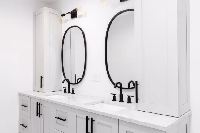A luxury bathroom with a grey double vanity cabinet, black faucets and lights, and a white marble countertop