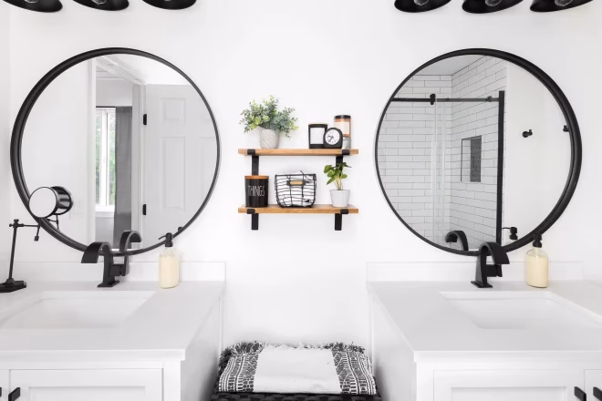 A modern farmhouse bathroom with a white vanity and marble countertop, circular black mirrors, and a view to the white subway tile shower.
