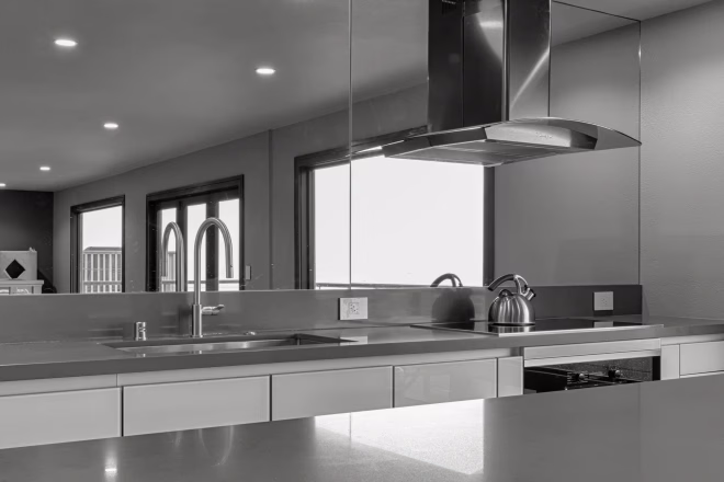 A modern kitchen design featuring a stainless steel range hood and gray countertops.