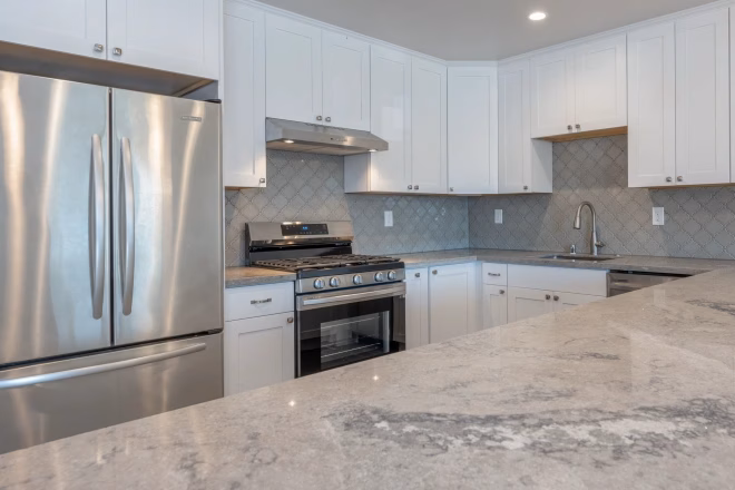 A remodeled kitchen with a granite countertop in the foreground and a gray tile backsplash