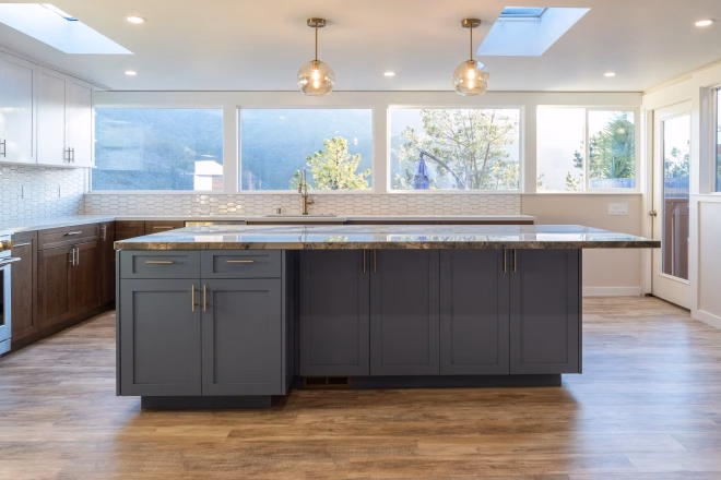 Large kitchen island with globe lights overhead and a stainless steel oven visible on the left in a newly remodeled kitchen