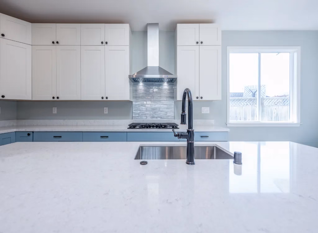 A silver colored tile backsplash in a renovated kitchen. A kitchen island with a sink is visible in the foreground.