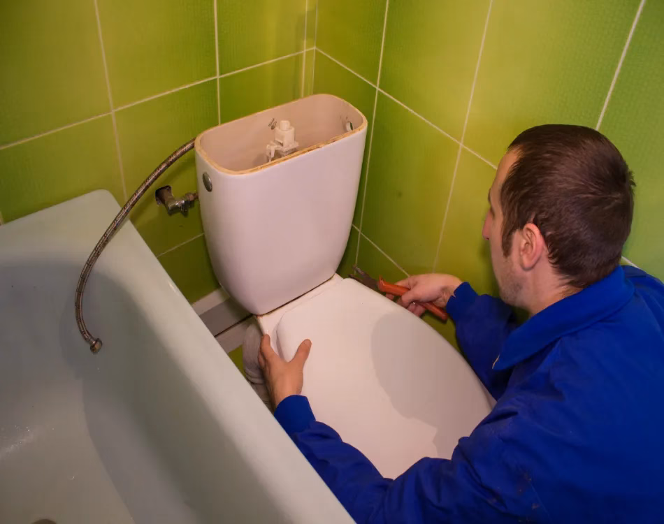 man unscrews a drain tank of a toilet